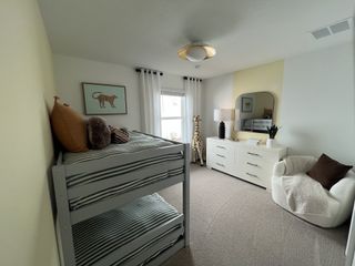 A cozy kids' bedroom features a bunk bed, plush armchair, dresser, and playful giraffe decor in a soft, neutral palette.