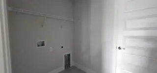 A laundry room with a sleek door, white walls, and shelving for efficient organization.