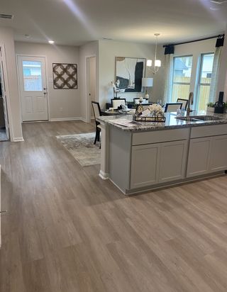 Model Home An open-concept kitchen with granite countertops, elegant dining area, and wood flooring creating a welcoming and modern space.
