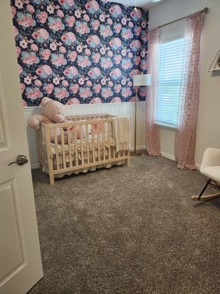 A charming nursery with floral wallpaper, cozy crib, and soft carpeting, creating a sweet ambiance for a little one.