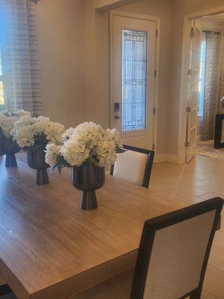 Model Home A chic dining area with a sleek wooden table, modern chairs, elegant floral centerpieces, and a stylish glass-paneled door.
