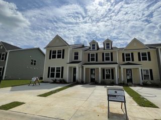 Street view A charming beige townhouse with dark shutters and a clean driveway in Hampton Woods by Dream Finders Homes (Summerville, SC).
