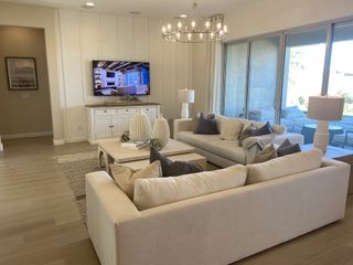 Model Home A bright living room with neutral tones features plush sofas, a statement chandelier, and sliding glass doors leading to an outdoor patio.