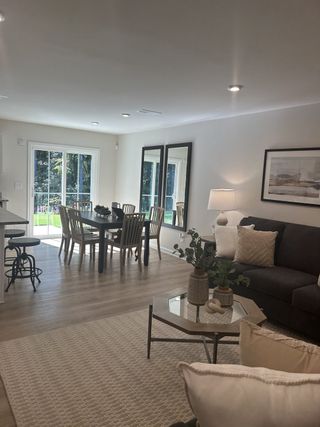 Model Home A bright, open-plan living space with cozy seating, a dining area, and large windows offering garden views.