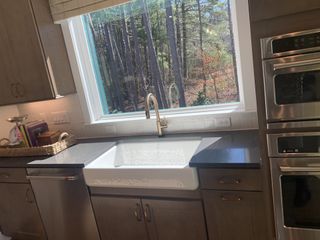 Model Home A beautiful kitchen with a farmhouse sink, dark countertops, stainless steel appliances, and a large window with a forest view.