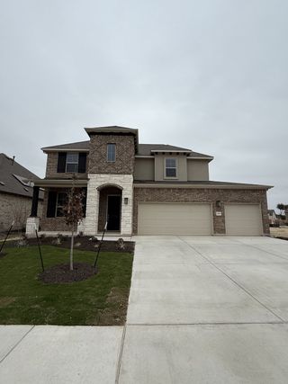 A modern brick home with a spacious driveway in Hawkes Landing by Brightland Homes (Leander, TX).