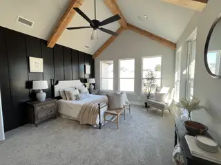 A spacious bedroom with vaulted wood-beam ceilings, dark accent wall, and cozy neutral decor.