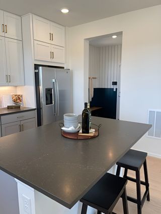 A modern kitchen with sleek gray countertop, white cabinets, stainless steel fridge, and stylish bar stools.