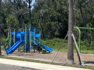Community Amenities A vibrant playground with blue slides and green accents in Wilford Oaks by Dream Finders Homes, Orange Park, FL.