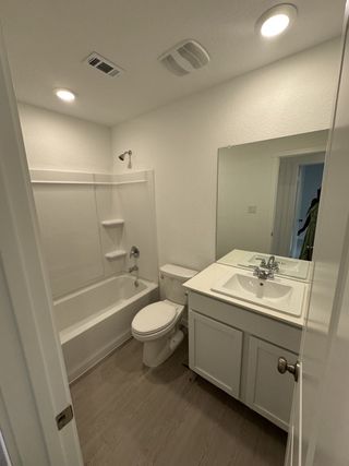Model Home A modern bathroom with a sleek white vanity, tub-shower combo, and warm wood-look flooring.