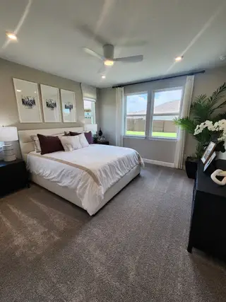 A cozy bedroom featuring neutral tones, a plush carpet, elegant decor, and abundant natural light through large windows.