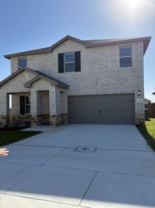 A modern two-story home with a white brick exterior, dark shutters, and a spacious two-car garage in Legendary Trails by Meritage Homes (Cibolo, TX).