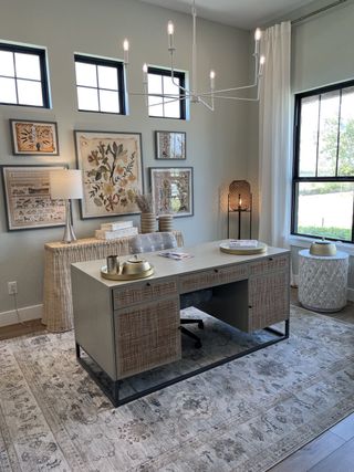 A chic home office with a modern desk, neutral decor, and nature-inspired artwork, complemented by large windows and elegant lighting.