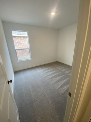 A cozy room featuring soft carpeting, pristine white walls, and a large window for natural light.