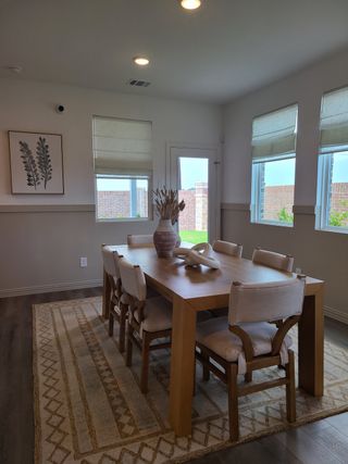 A cozy dining room with a wooden table, cushioned chairs, and natural light from wide windows, creating a warm ambiance.