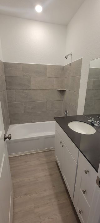 A chic guest bathroom with a dark vanity, light wood flooring, and a bathtub with elegant gray tile walls.