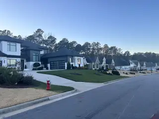 Street view Modern homes with manicured lawns in Montvale at Copperleaf by Upright Builders, set amid lush greenery in Cary, NC.