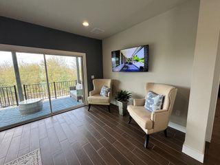 Model Home A cozy seating area with elegant armchairs, a mounted TV, and a view to a balcony through sliding glass doors.
