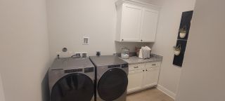 Model Home A sleek laundry room with modern appliances, white cabinets, and granite countertops, accented by wall decor and potted plants.