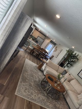 A cozy living room with a plush sectional, patterned rug, and an open view of the dining and kitchen area.
