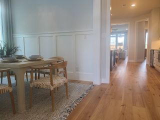 A modern dining area with a light wood table, cozy woven chairs, and elegant paneling, leading to an open-living space.