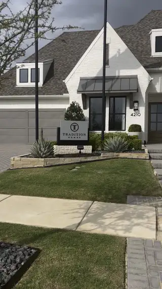 Street view A stylish white brick home with lush landscaping at Mustang Lakes – 100′ by Tradition Homes in Celina, TX.