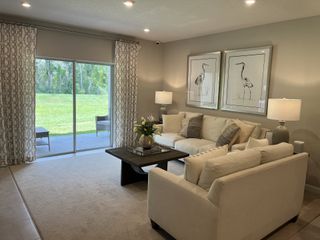 A cozy living room with neutral sofas, nature-inspired art, and a view of the lush outdoors through sliding glass doors.