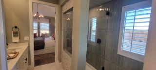 Model Home A modern bathroom with a sleek shower, tiled walls, and a view into a bright, cozy bedroom with elegant lighting.