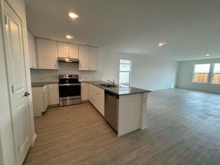 A modern kitchen with stainless steel appliances, white cabinets, and an open concept leading into a bright living area.