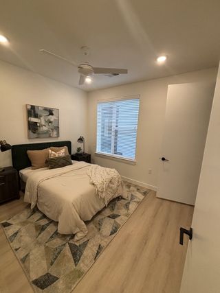 Model Home A cozy bedroom with warm lighting, a plush bed, abstract art, and a geometric rug on wooden flooring.