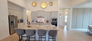Model Home A bright, open kitchen with a large island, gray cabinets, and unique wall decor, in a Stillwater Ranch home by Coventry Homes (San Antonio, TX), blending style and space.