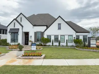 Street view A charming white brick home with manicured landscaping in Grange by Highland Homes, located in Katy, TX.