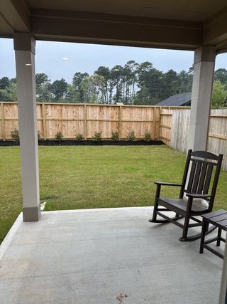 Model Home A cozy patio with a wooden rocking chair and a spacious fenced backyard view, perfect for relaxation.