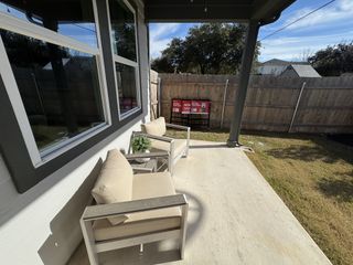 A cozy patio with beige cushioned chairs, a small table, and a fenced yard offering a private outdoor retreat.