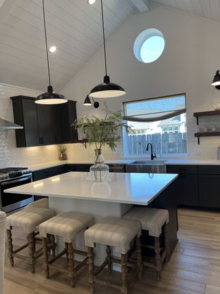 A modern kitchen featuring a vaulted ceiling, island with seating, black cabinetry, and industrial pendant lighting.