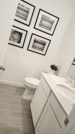 A bright powder room with a white vanity, framed wall art, and sleek tile flooring for a fresh and modern touch.