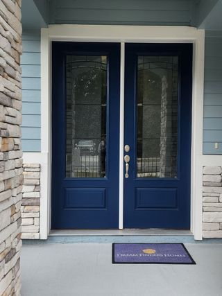 Street view A welcoming blue front door with elegant glass panels and stone siding in Wilford Preserve by Dream Finders Homes (Orange Park, FL).