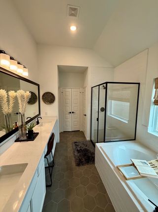 A modern bathroom with dual sinks, white countertops, hexagonal tile flooring, and a glass-enclosed shower, featuring a separate soaking tub.