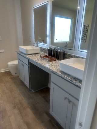 A modern bathroom with dual vessel sinks, granite countertops, and sleek wooden flooring.