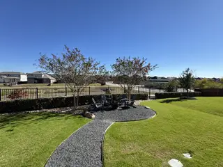 A spacious grassy backyard with a gravel path and cozy seating area in Sunfield by Pulte Homes (Buda, TX).