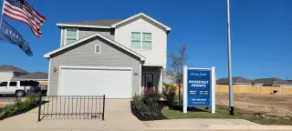 Street view A modern gray home with a double garage, flag display, and landscaped front in Roosevelt Heights by Starlight Homes (San Antonio, TX).