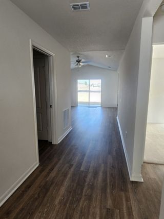 Model Home A bright, open hallway with wood-style flooring, recessed lighting, and a view into a sunny living area with sliding glass doors.