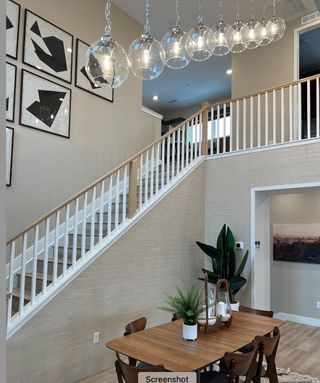 A modern dining area with a wooden table, contemporary lighting, geometric art, and an elegant staircase.