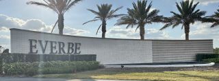 Community Amenities A modern entry sign surrounded by lush landscaping and palm trees at EverBe: Venture Townhomes by Lennar in Orlando, FL.