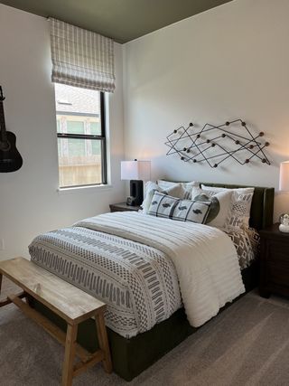 Cozy bedroom with decorative wall art, patterned bedding, and a wooden bench, featuring a guitar for a touch of personality.