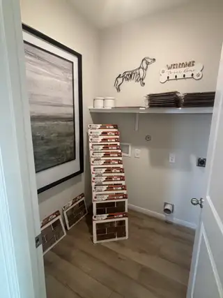 A cozy utility room featuring dog-themed decor, a large landscape print, and stacked tile samples on wood flooring.