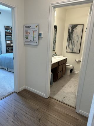Model Home A cozy hallway with wood flooring, leading to a bathroom with tiled floors, stylish artwork, and a neatly organized vanity.
