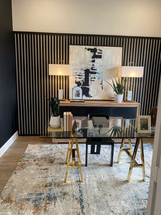 Model Home A chic home office with a modern abstract painting, glass desk, stylish lighting, and a textured rug.