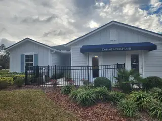 Street view A charming blue-shuttered home with lush landscaping in Dunns Crossing by Dream Finders Homes (Jacksonville, FL).