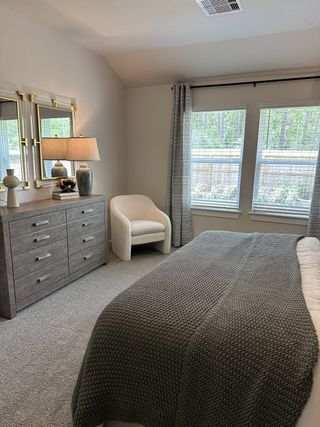 A cozy bedroom with a plush chair, modern gray dresser, and soft lighting from a stylish lamp.